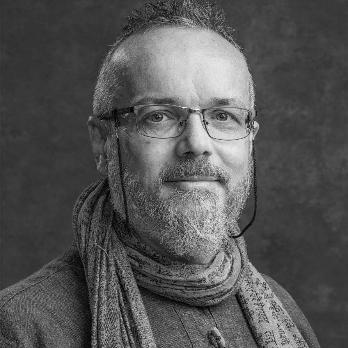 Porträt von Marek Stejskal mit Brille, grauem Bart und gemustertem Schal, freundlich in die Kamera blickend.